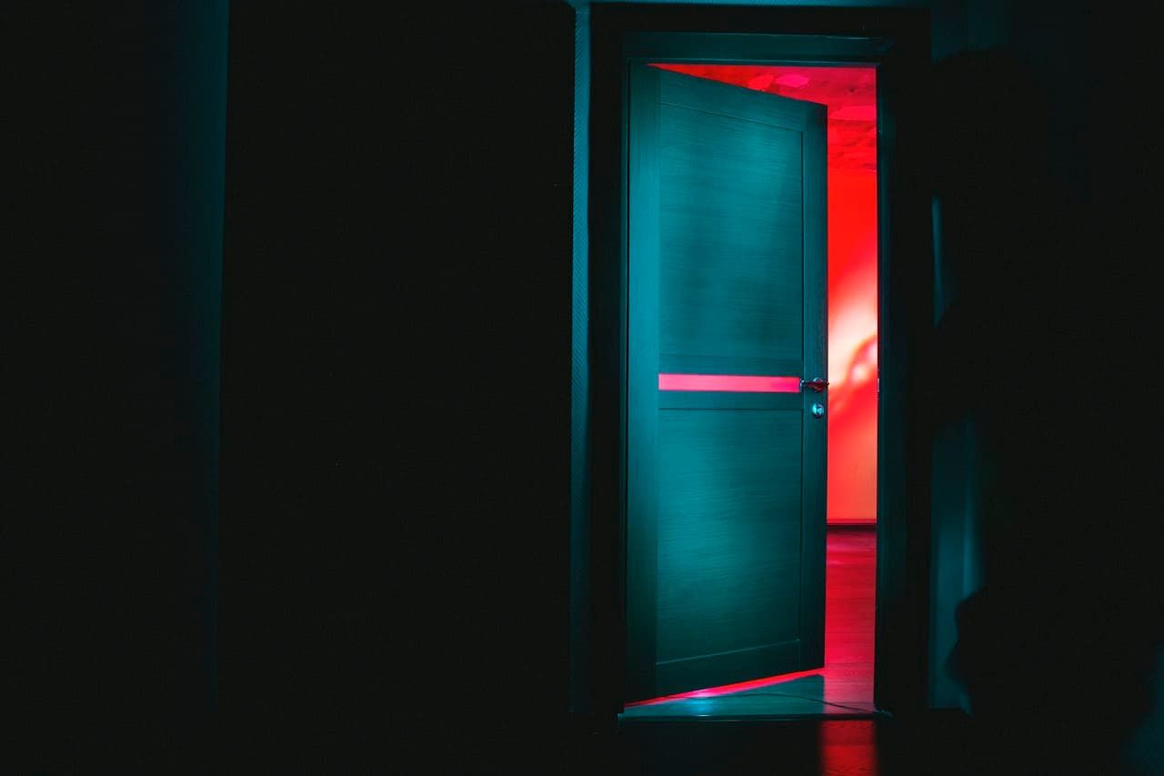 Porte entrouverte révélant une pièce rouge dans l'obscurité